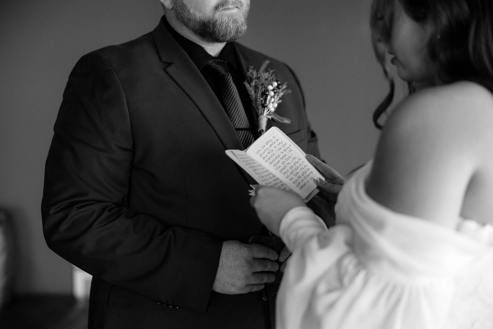 A black and white photo of a couple exchanging vows during their wedding ceremony.