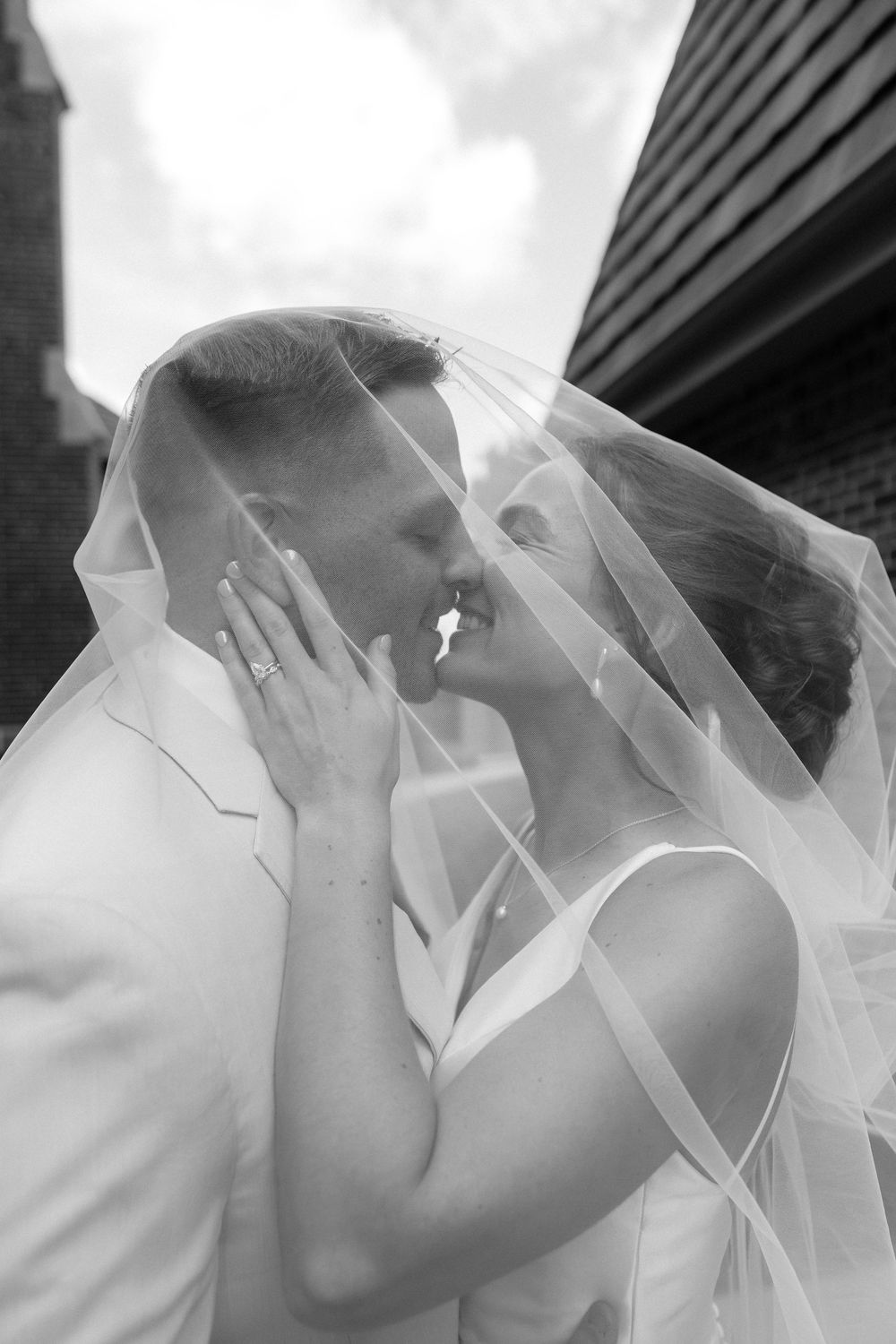 A romantic black and white photograph sequence showing newlyweds sharing a kiss under a flowing wedding veil.