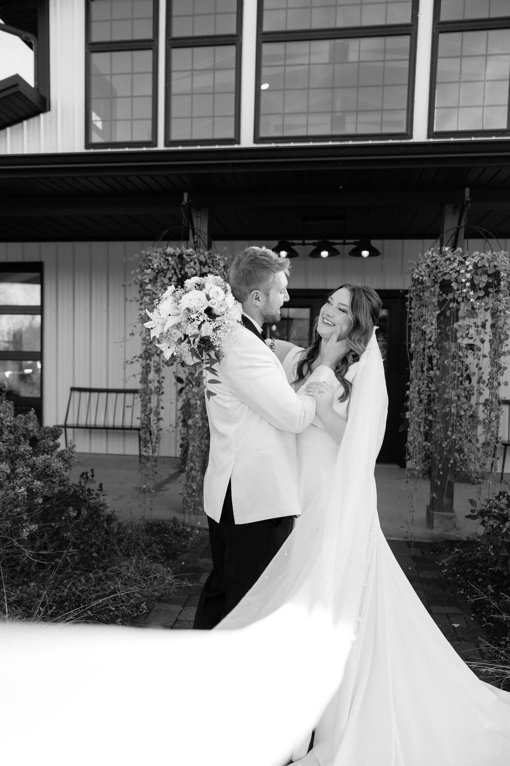 A romantic black and white wedding photo of a couple sharing a joyful moment outside a modern venue.