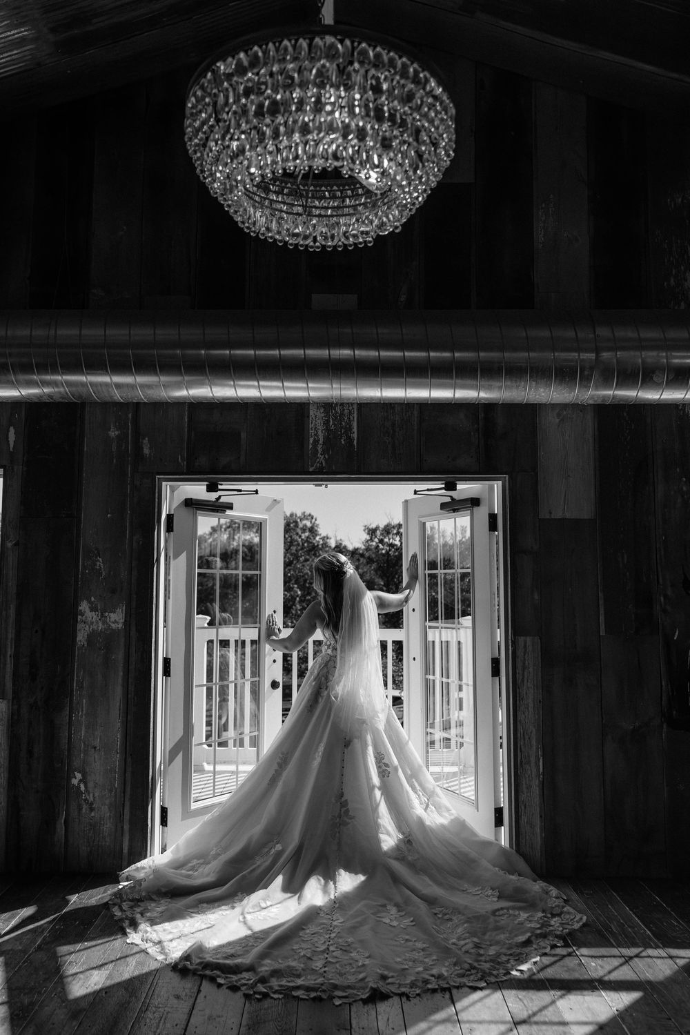 Wedding dress silhouettes displayed in a barn venue with dramatic backlighting through French doors and elegant chandeliers.