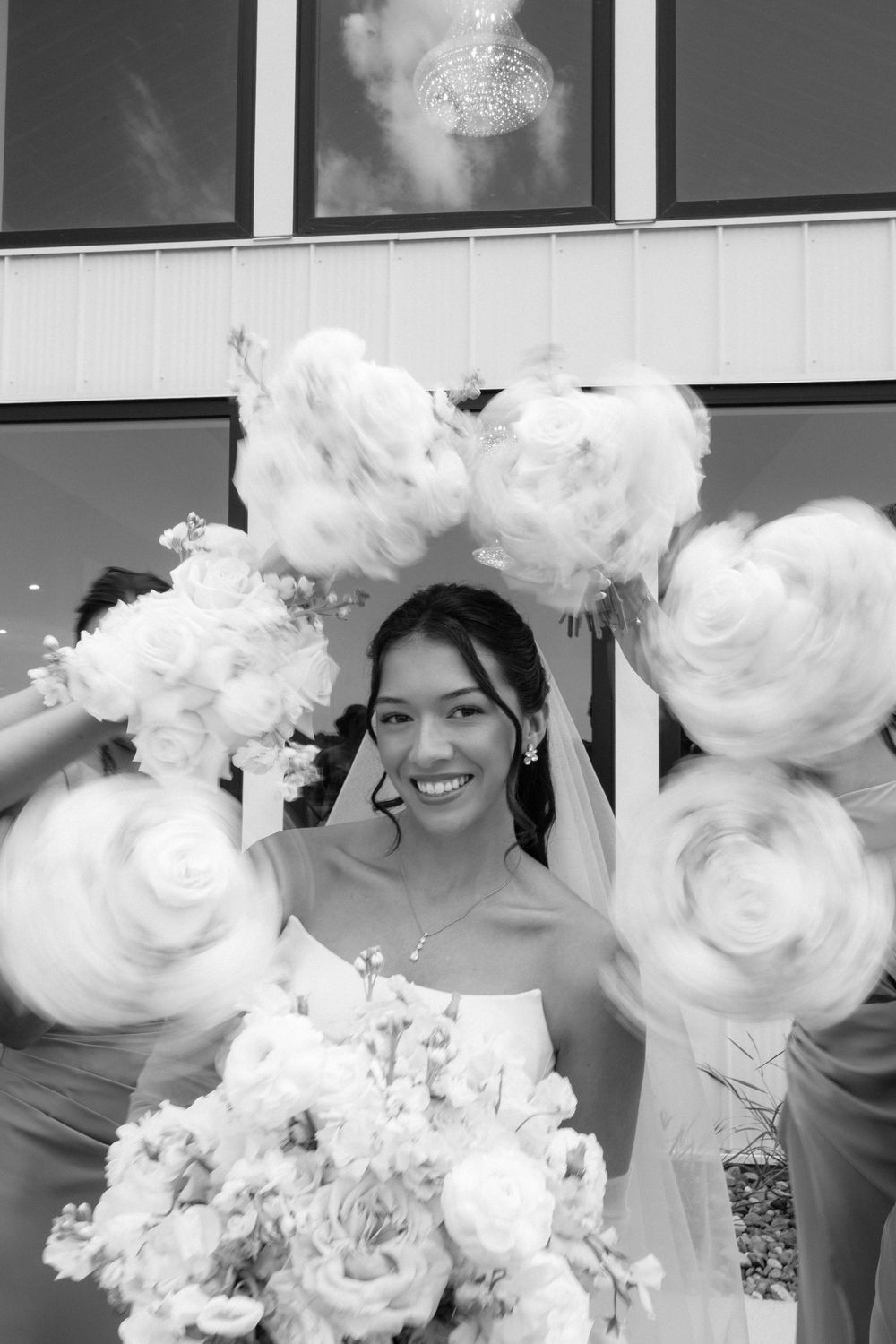 Black and white photo of a smiling bride surrounded by bridesmaids holding bouquets in a circular frame around her.