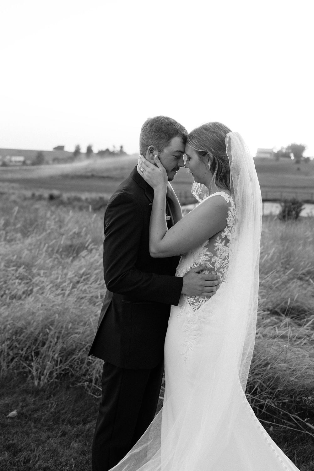 Black and white romantic wedding portraits of a couple embracing in a rustic field setting.