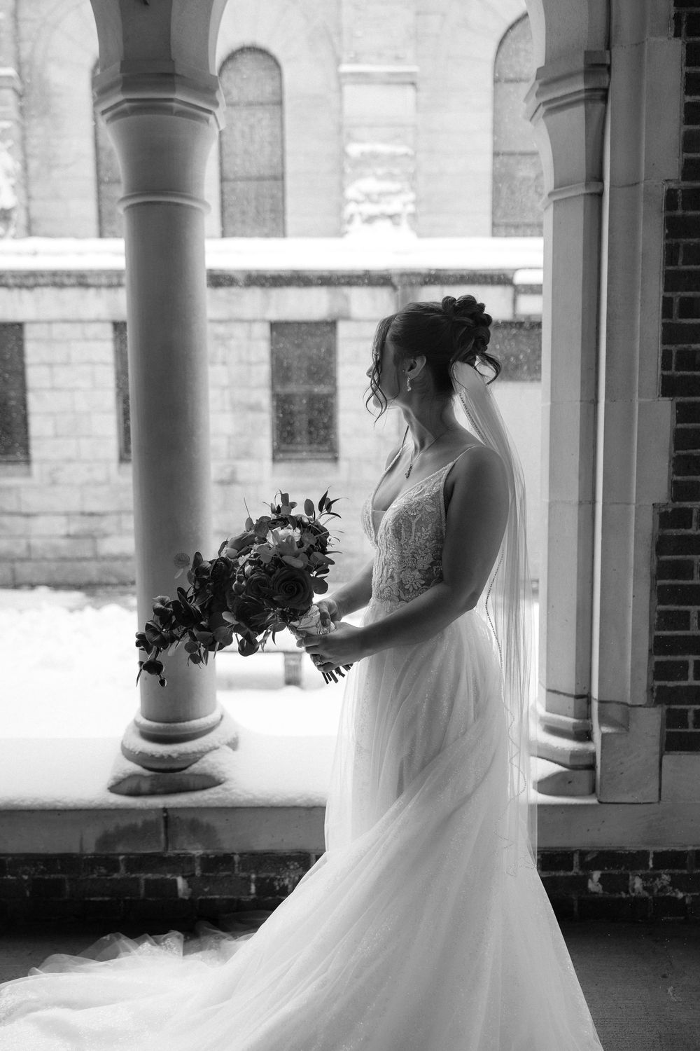 A black and white wedding photo series showing a bride in a flowing white dress posing between elegant stone columns.