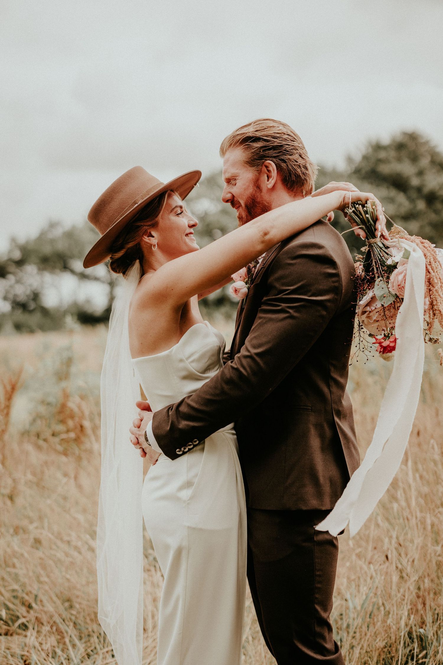 A romantic wedding moment captured in a golden field as a couple in formal attire share an intimate embrace.