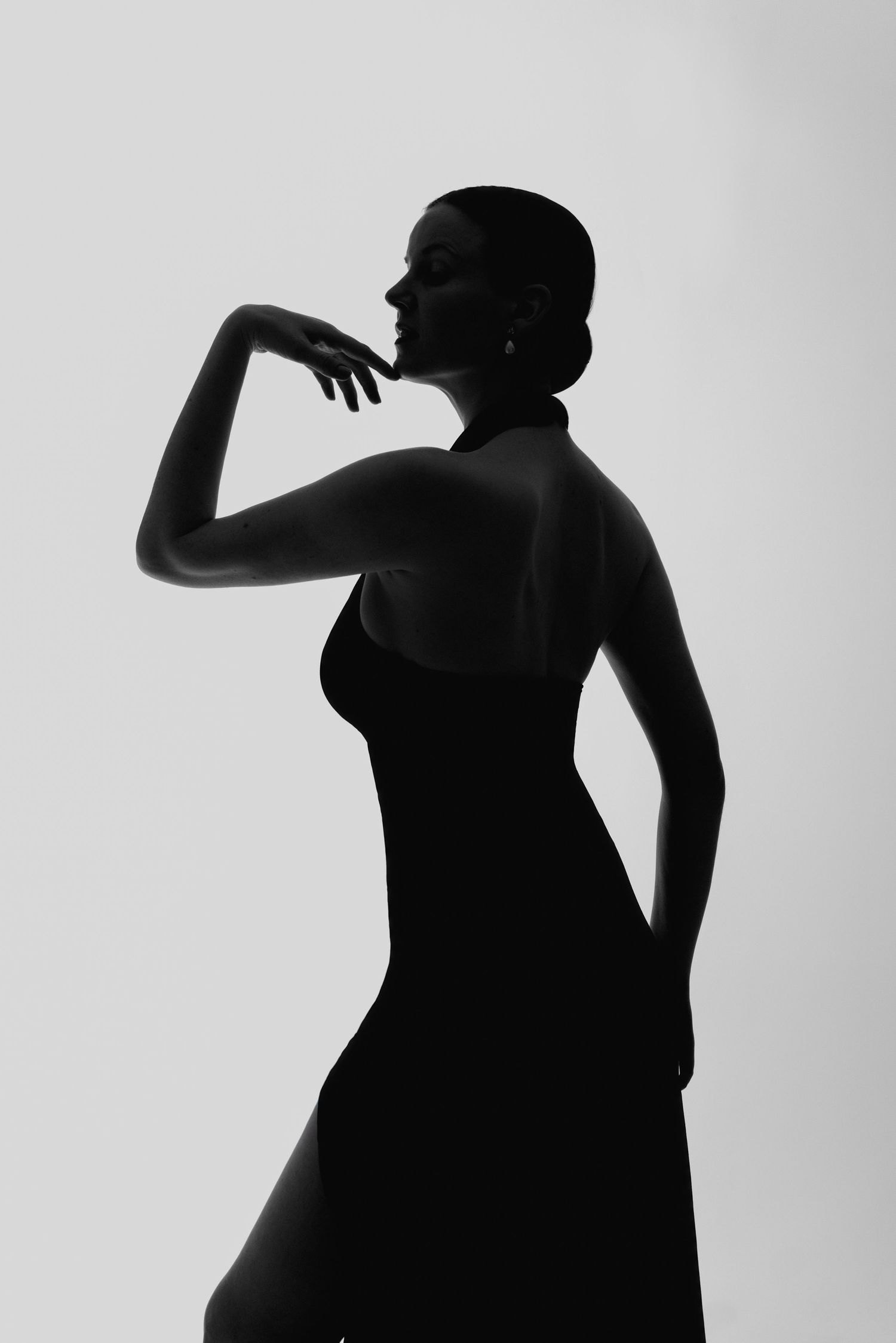 Elegant black and white silhouette of a woman in a sleek halter dress, posed gracefully against a light background.