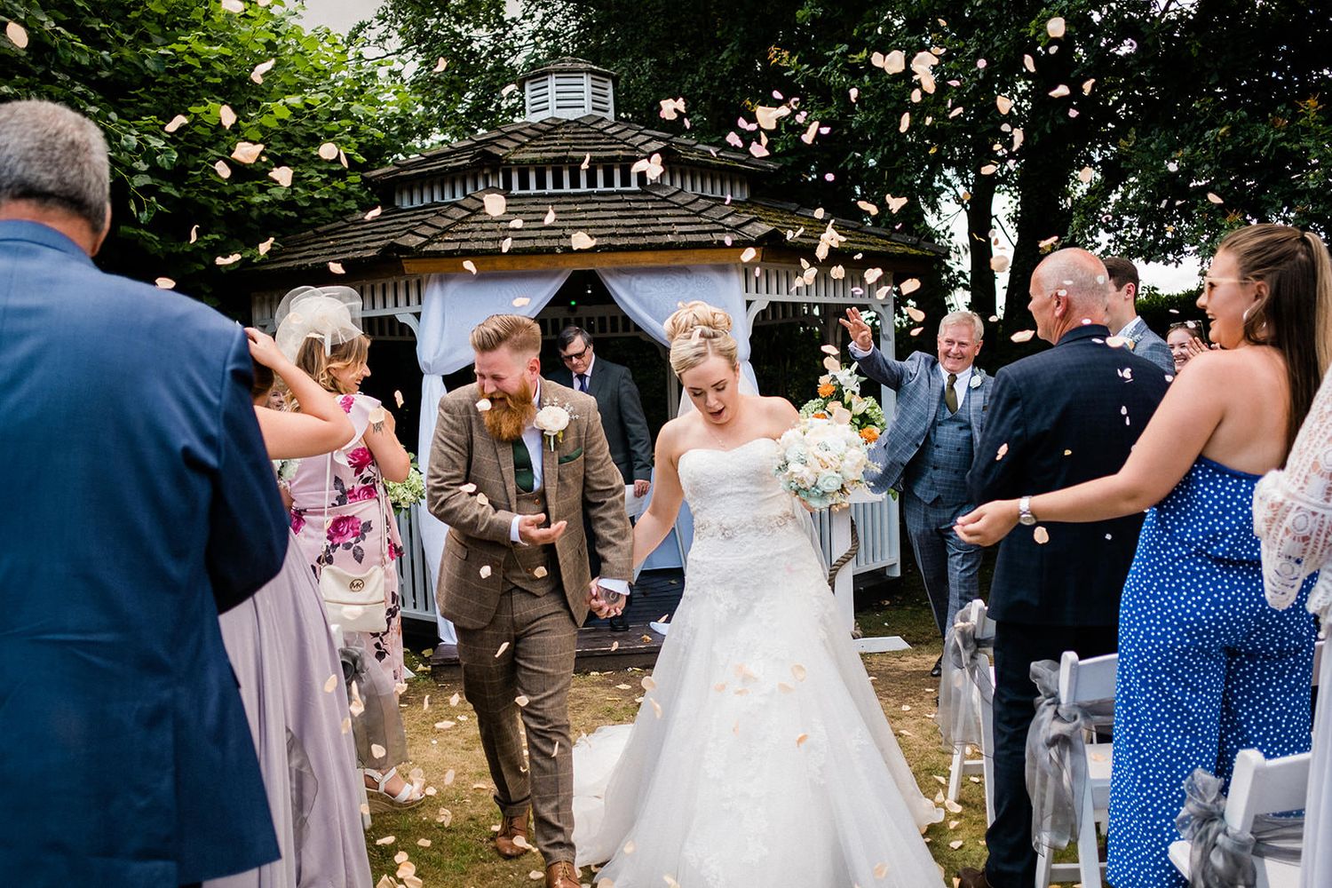 Wedding ceremony exit with guests throwing confetti at newlyweds outside a gazebo.