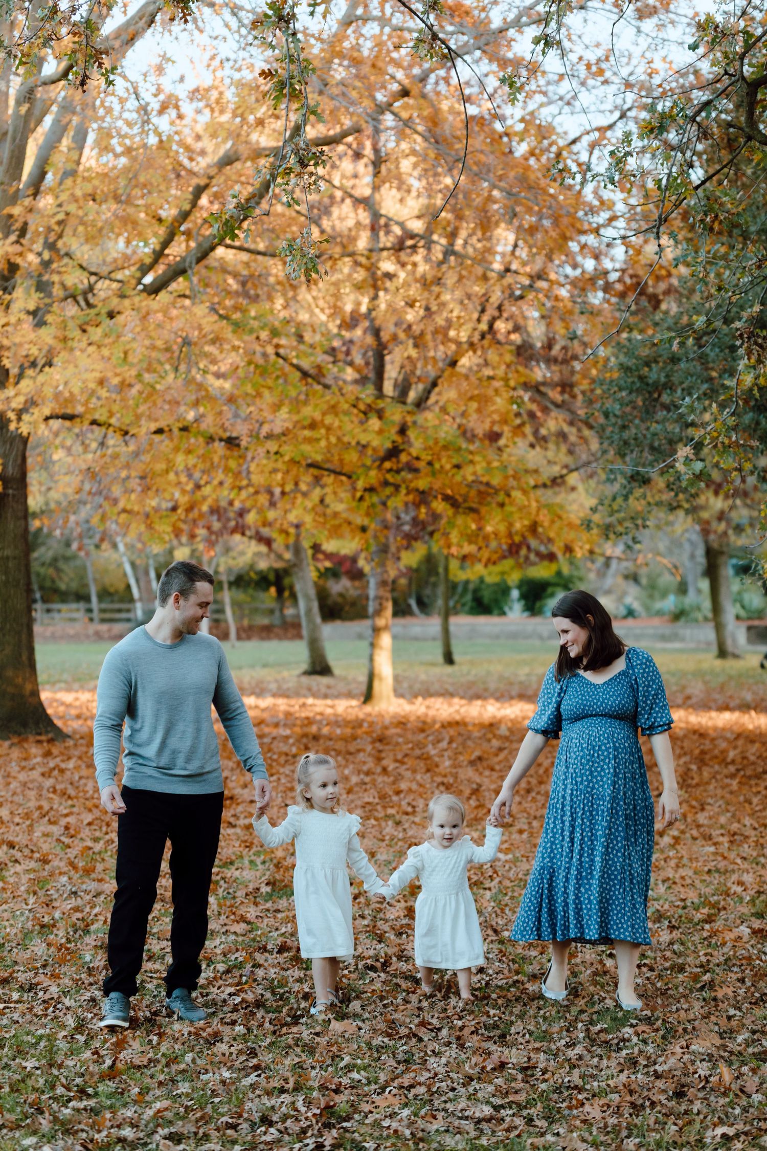 A family walks together through a park filled with golden autumn leaves.