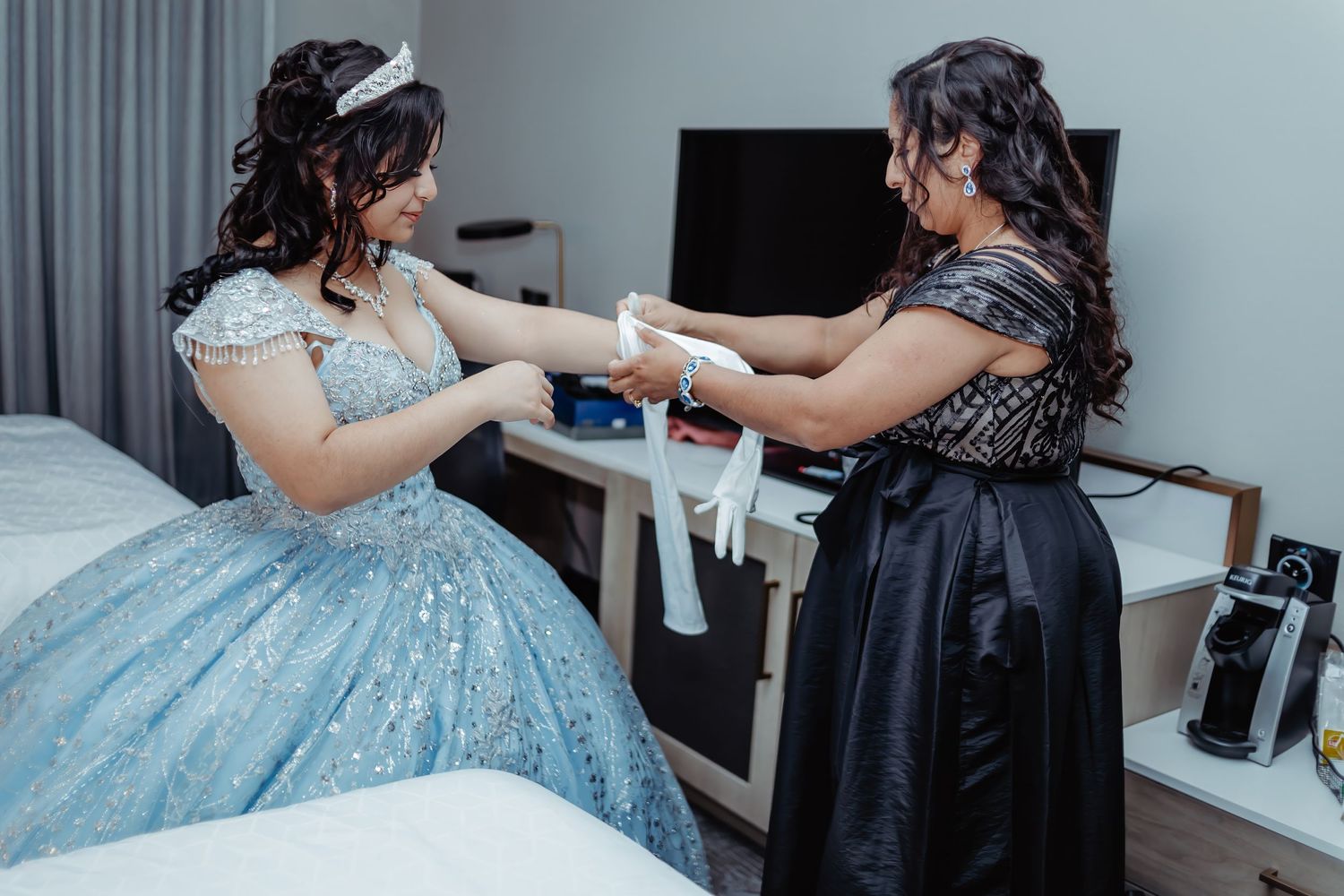 Two people in formal dresses, one blue and one black, share a celebratory moment indoors.