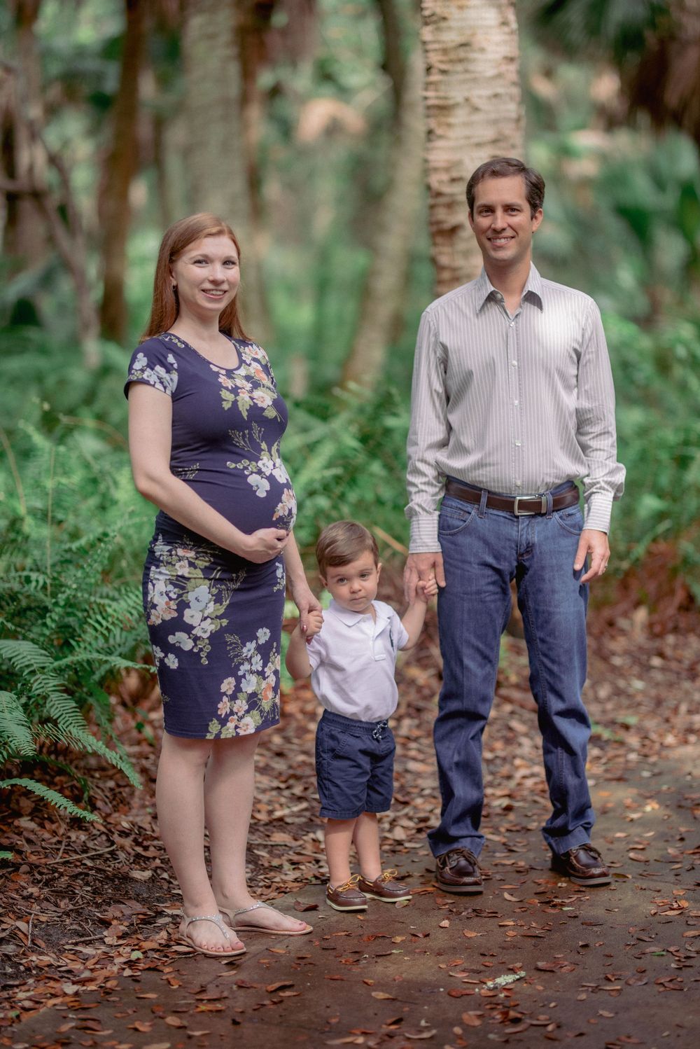 A young family poses on a wooded path with tall palm trees in the background.