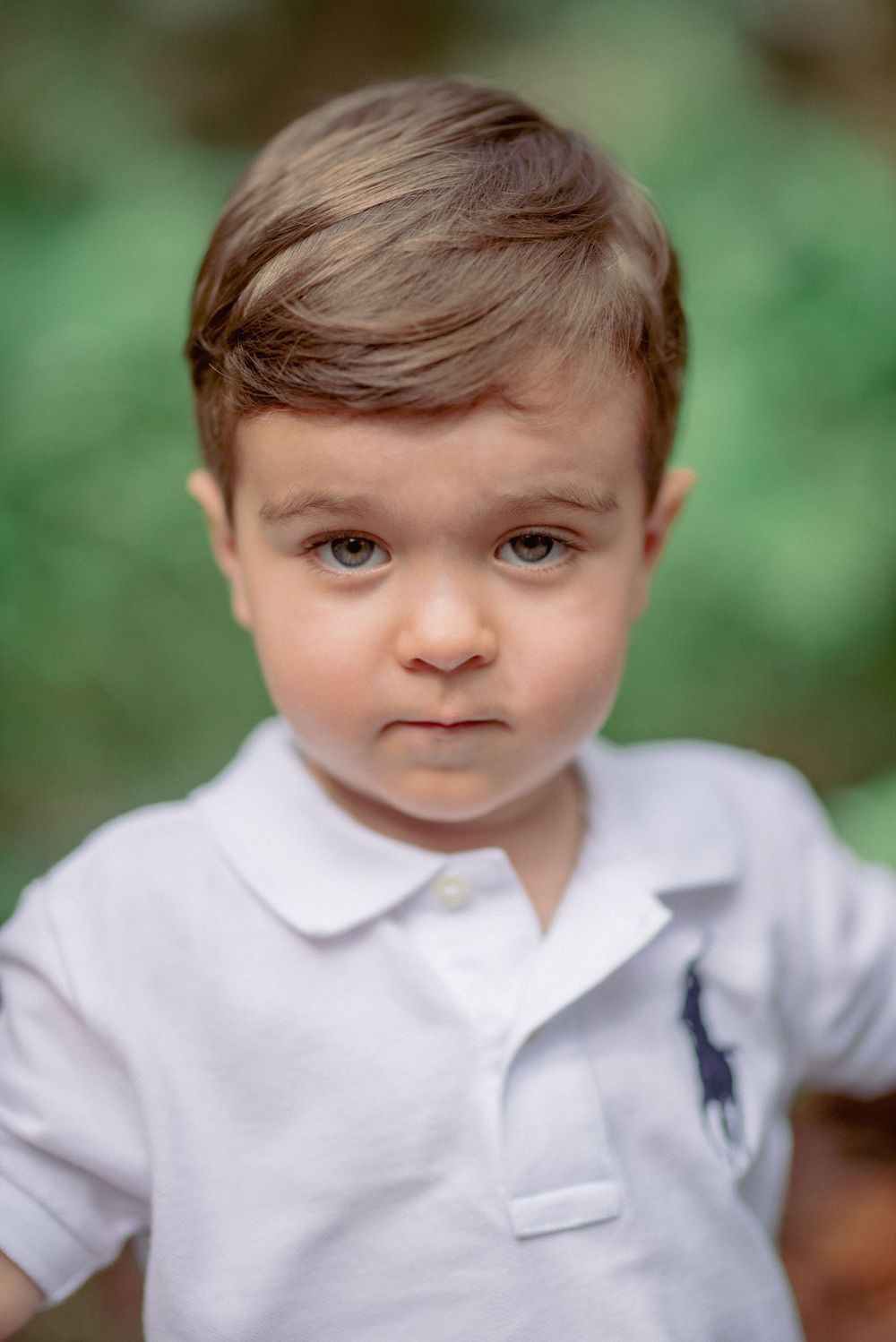 A young child in a white polo shirt poses for a close-up portrait outdoors.