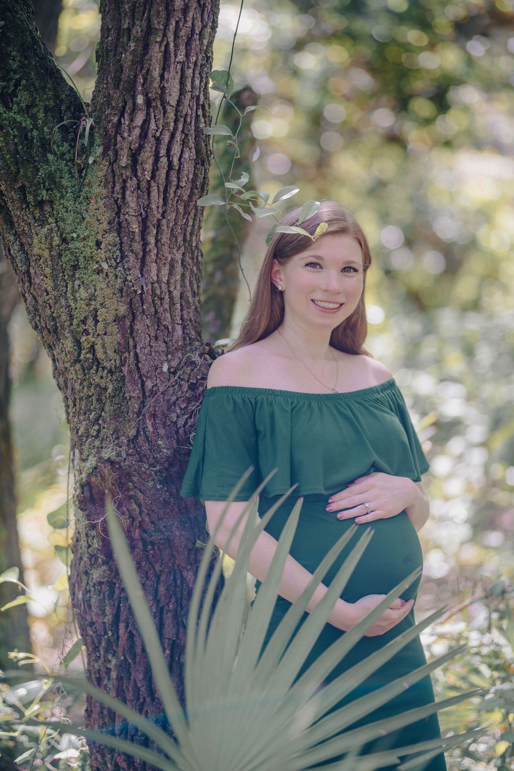 A maternity photoshoot in a green forest setting with palm fronds.