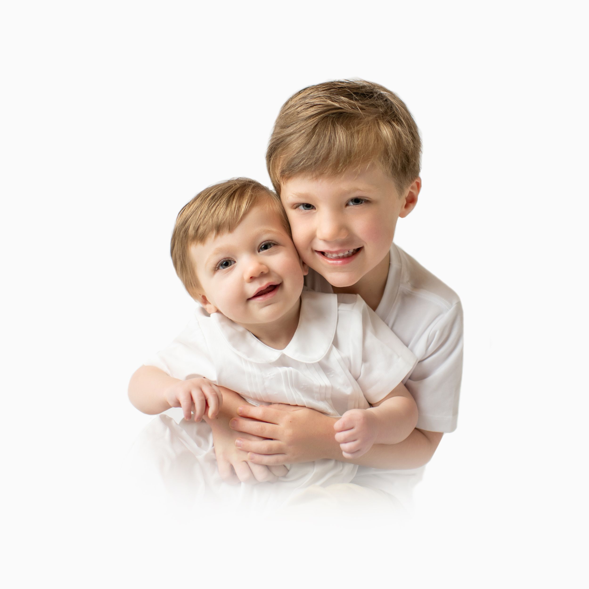 Two children in white shirts embracing and laughing against white background.