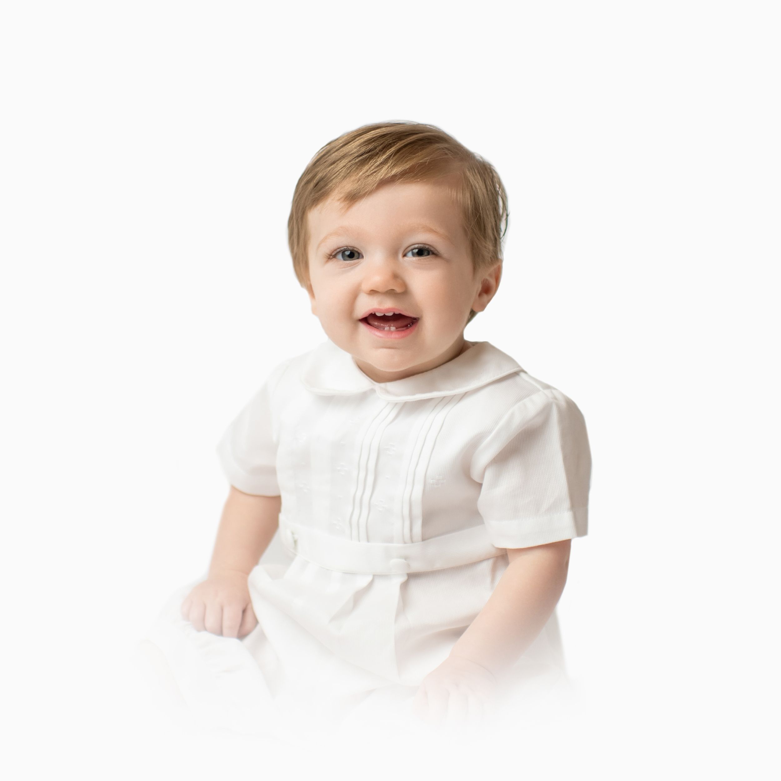 Toddler in white shirt smiling against white background.