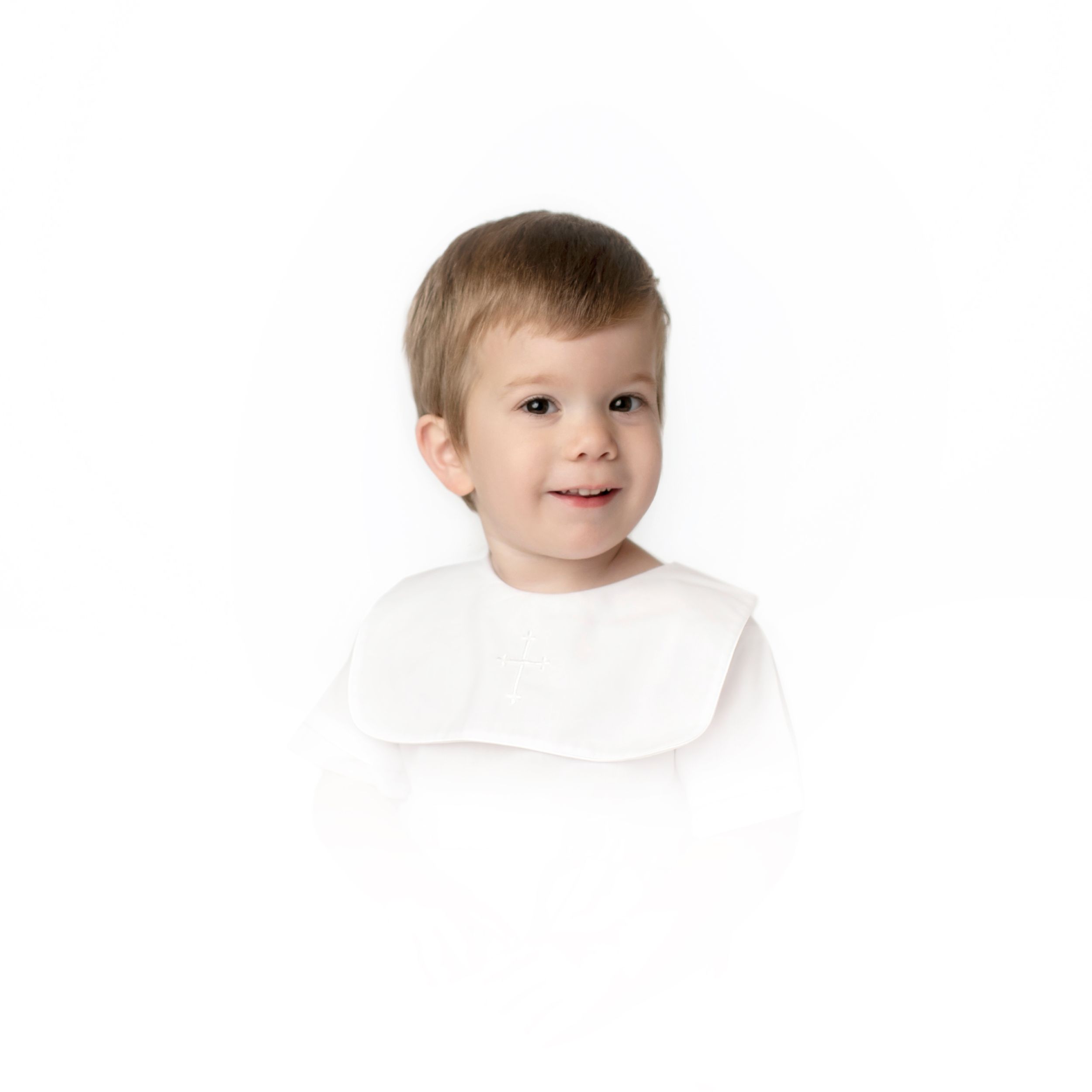 Young child in white bib smiling at camera against white backdrop.