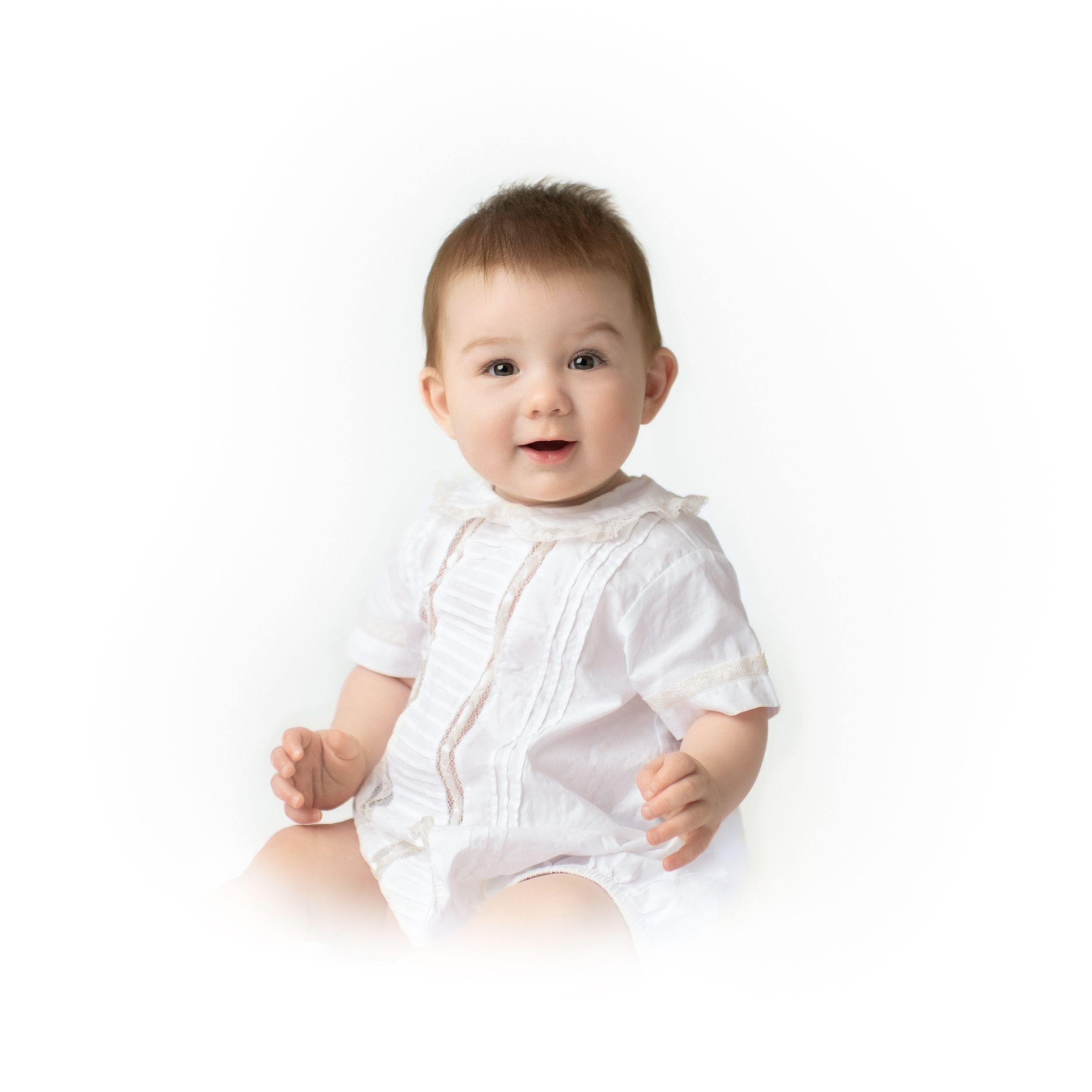 Baby in white embroidered outfit against white background.