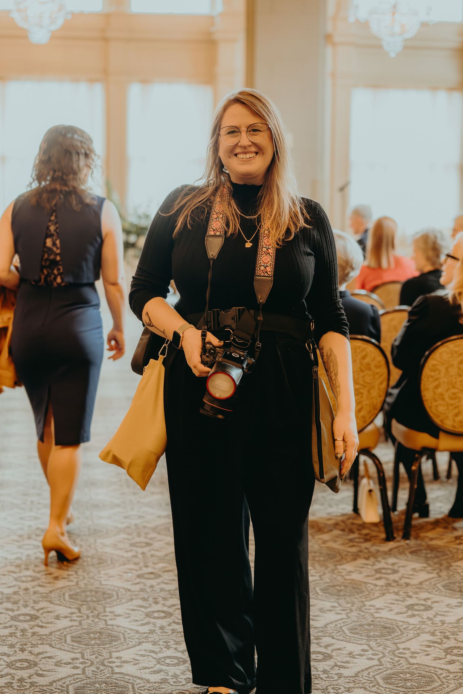A person in a black outfit walks through an elegant room with ornate chairs and decor in warm lighting.