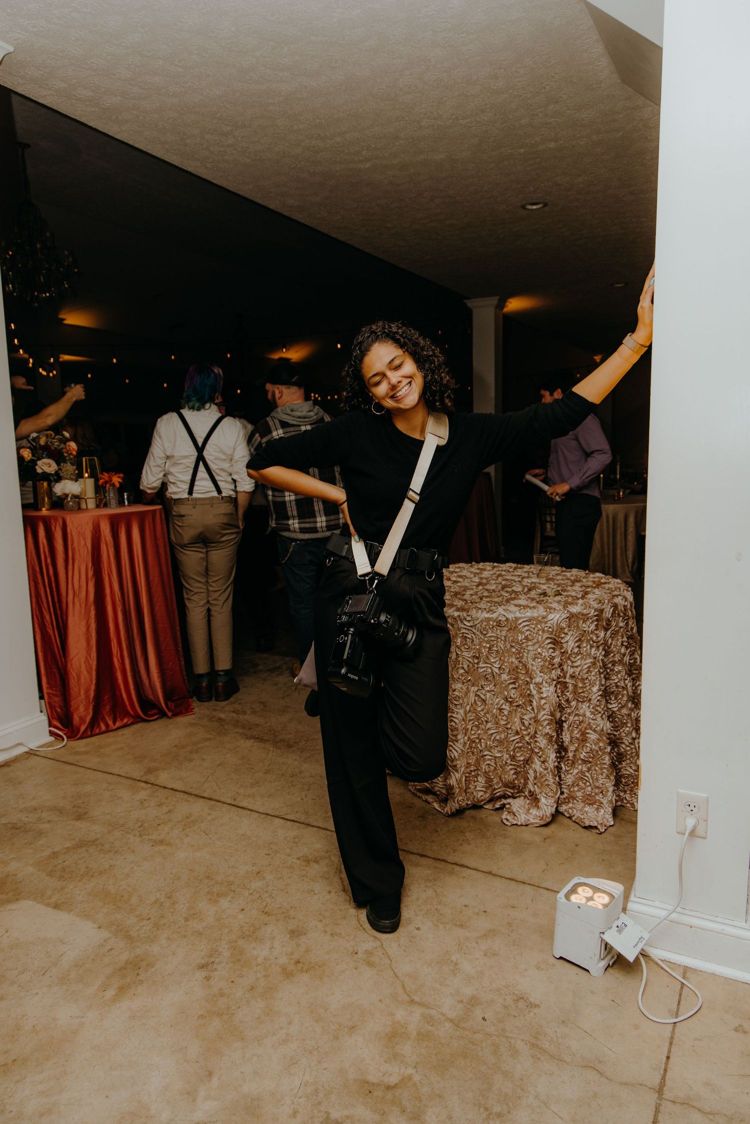 A person dances energetically at a reception venue with decorative tablecloths and curtains visible in the background.