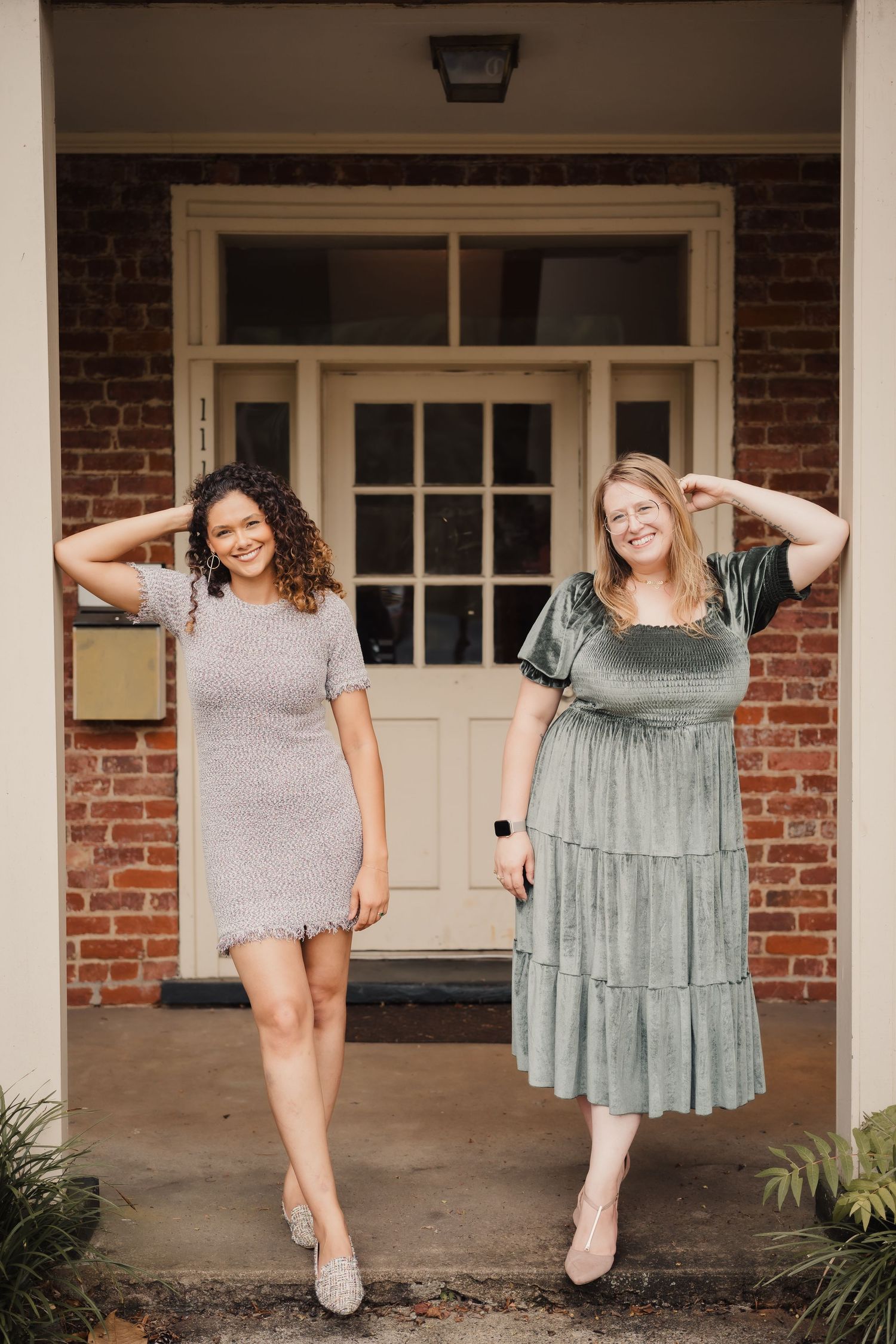 Two photographers striking fun poses on a brick building porch.