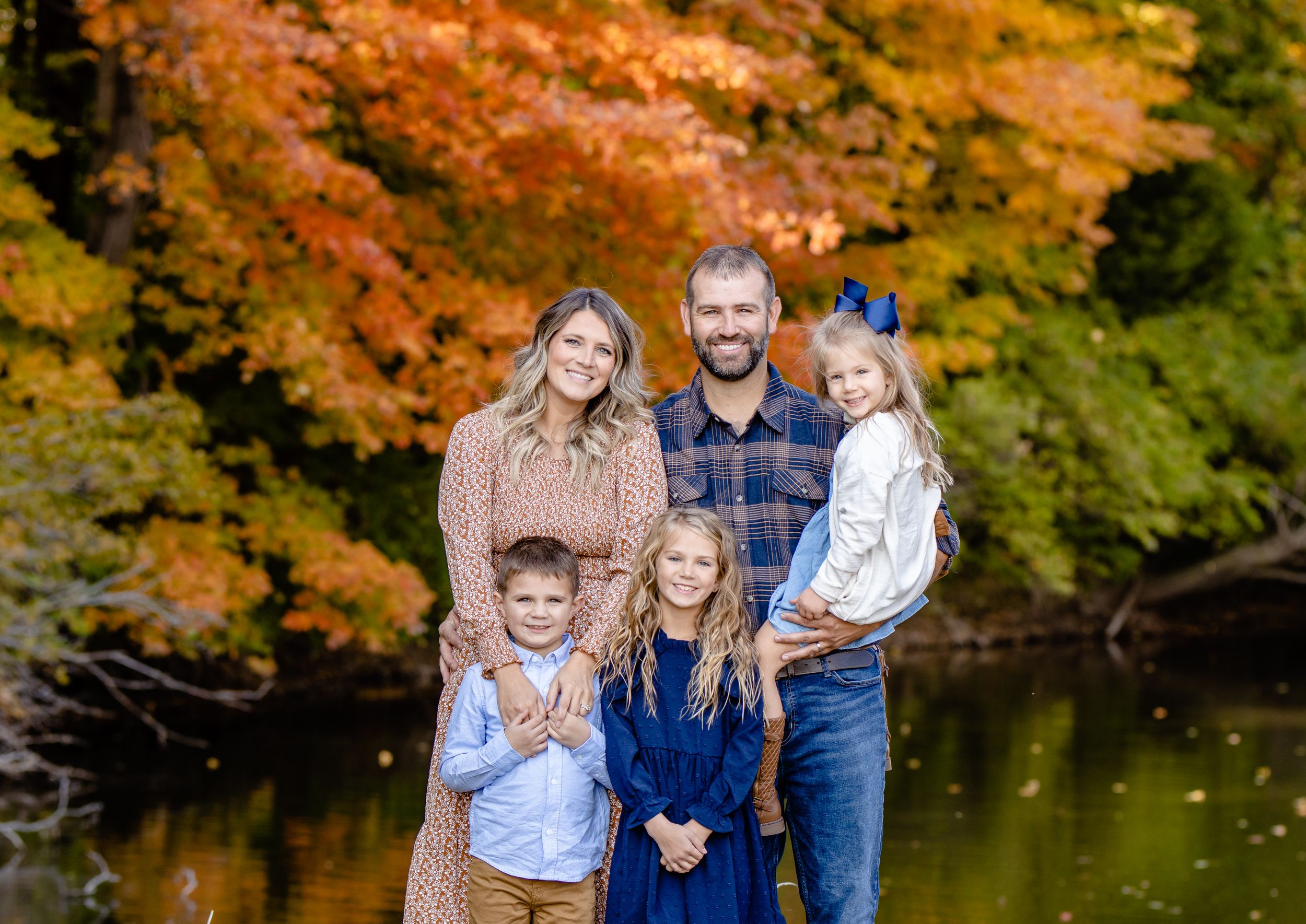 Family portrait with vibrant fall foliage and a reflective pond in the background.