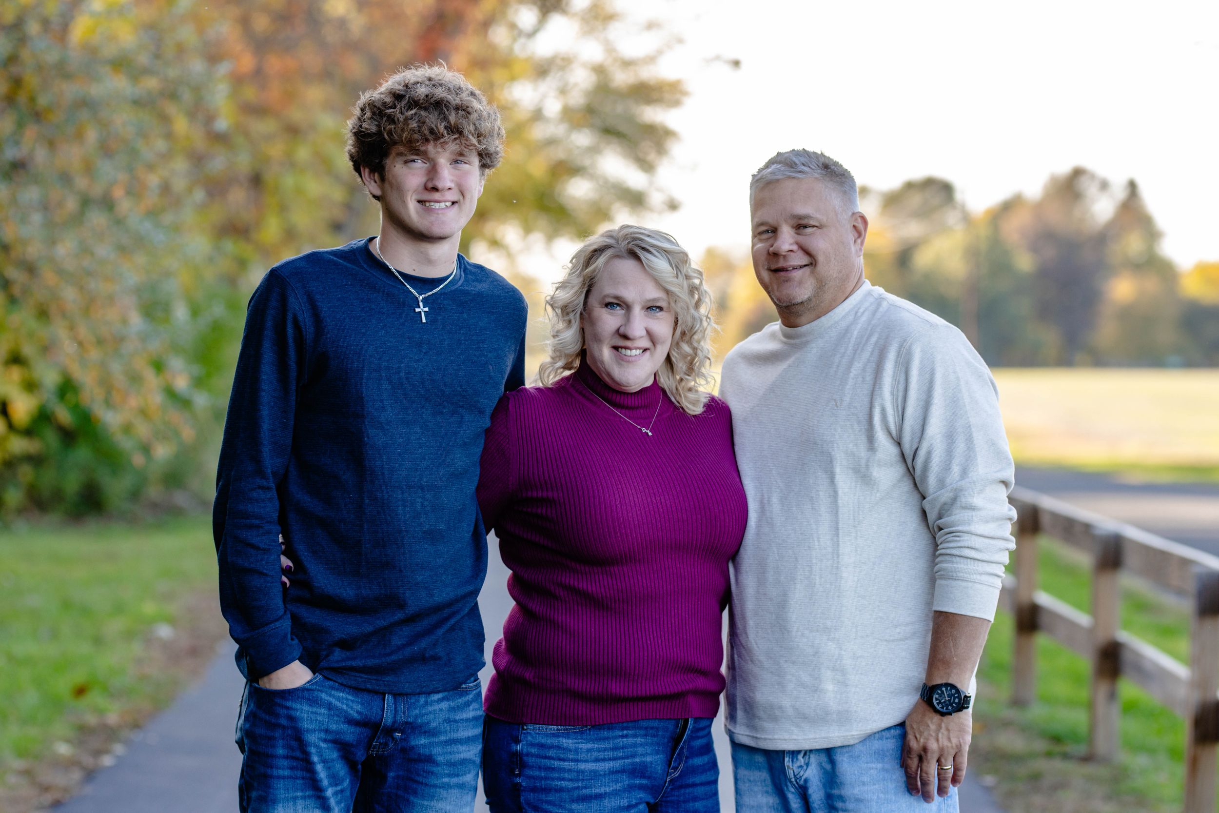 Three people pose together outdoors during autumn photo session.