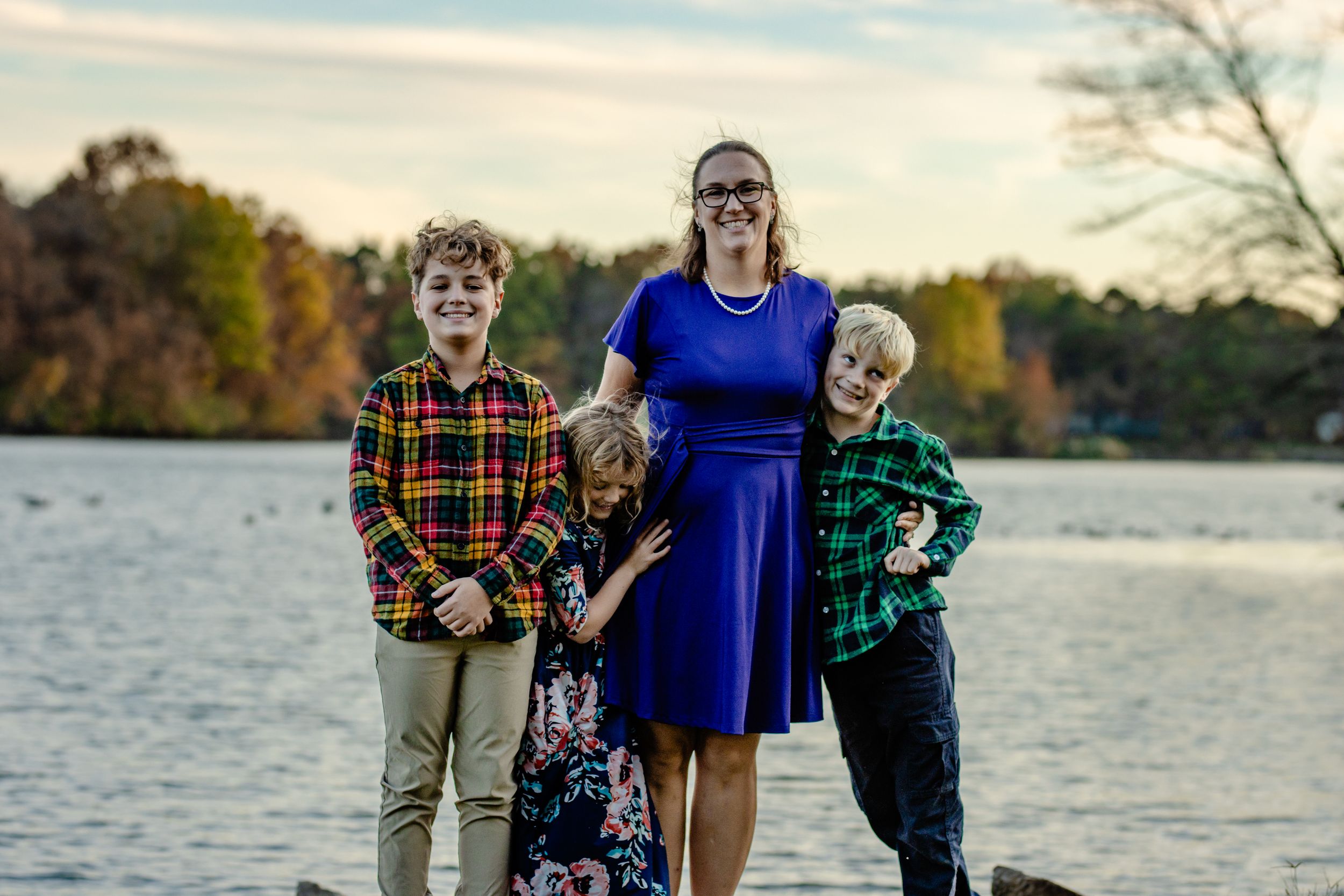 Family portrait by lake at sunset with fall trees in background.