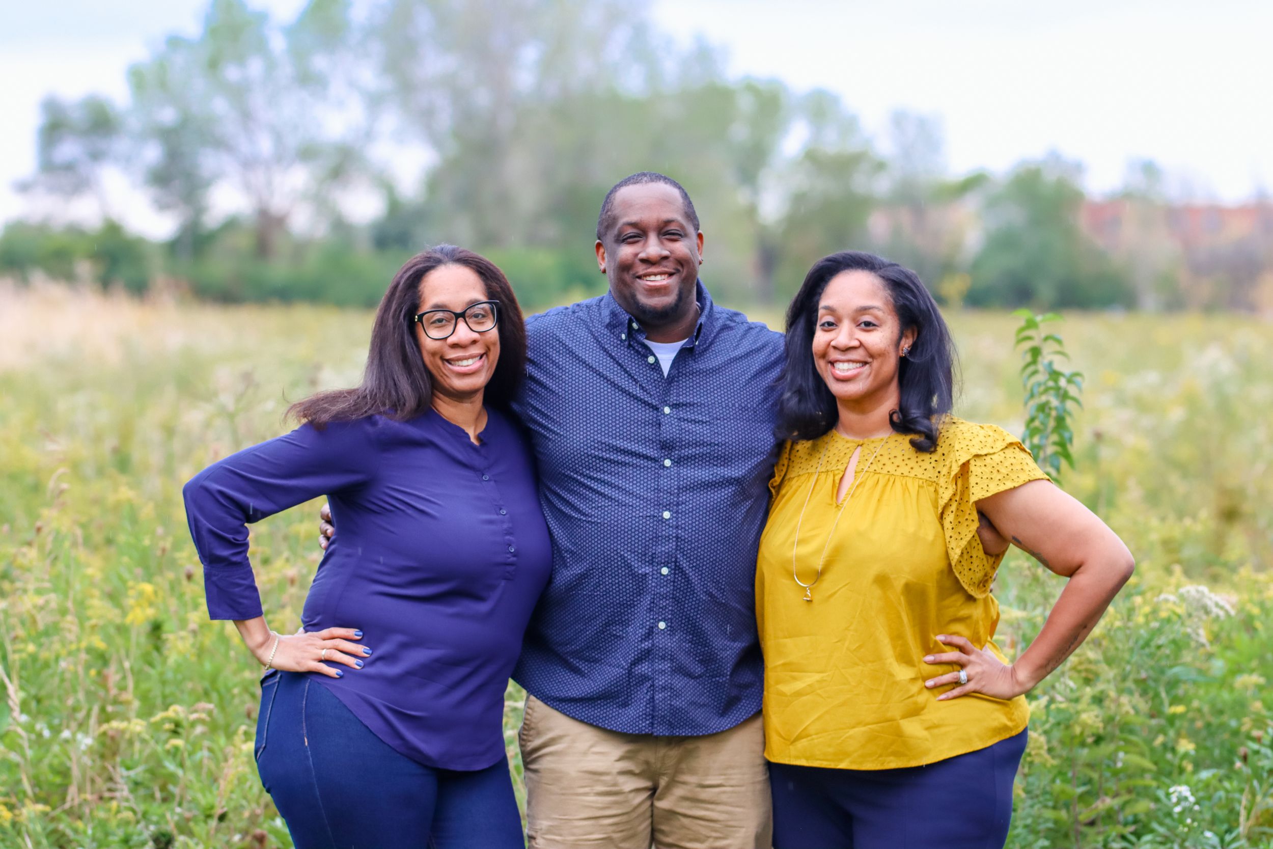 Three friends smiling together during outdoor portrait session in field.