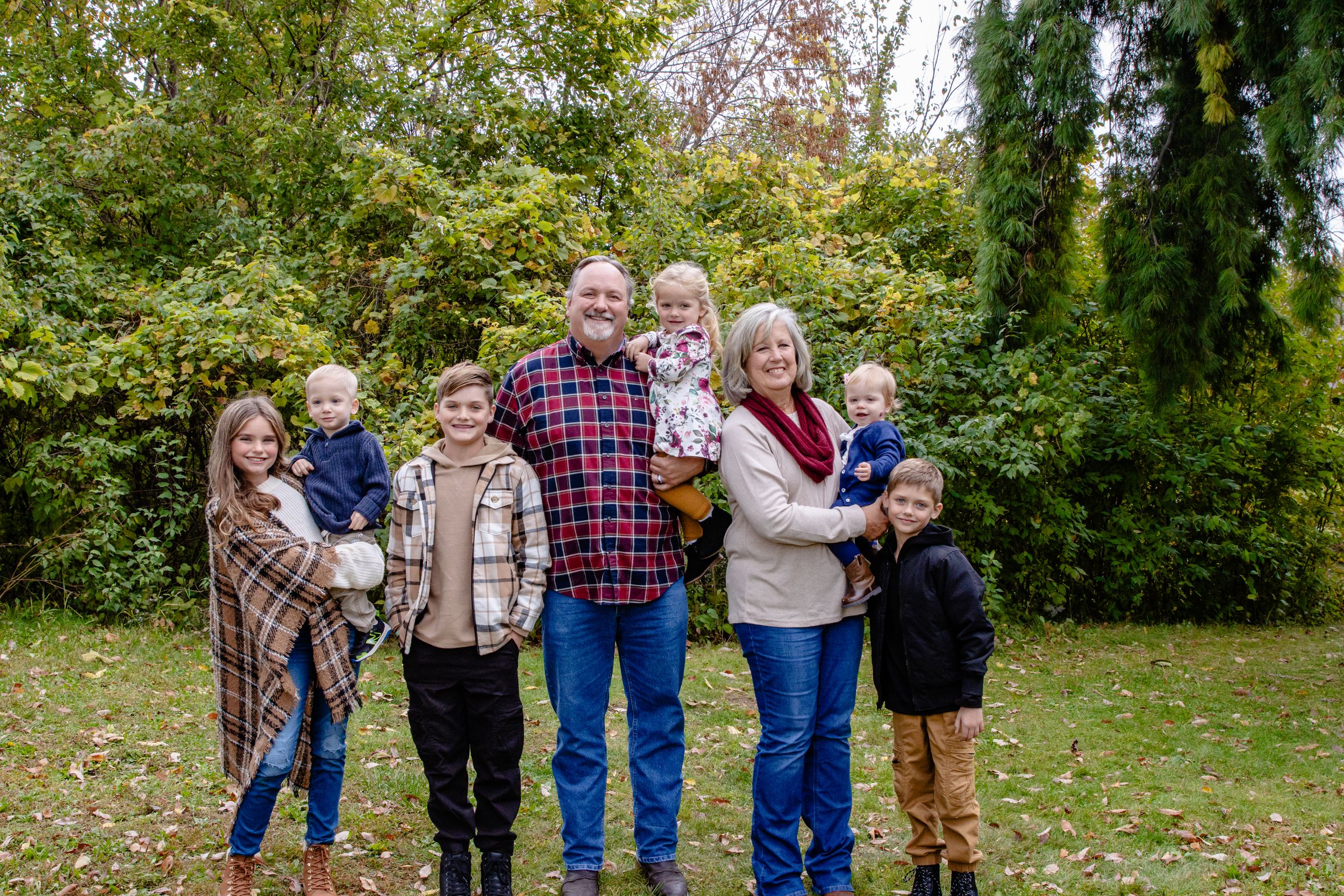 Group photo of family members standing together on grass with fall foliage in background.