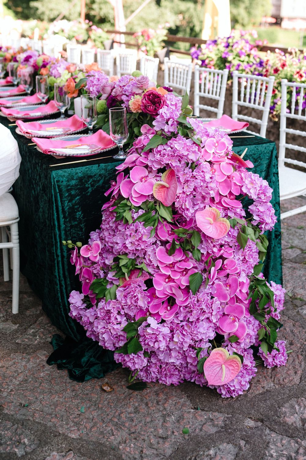 Elegant table setting with emerald velvet tablecloth and lush pink hydrangea and rose floral arrangements for a wedding reception.
