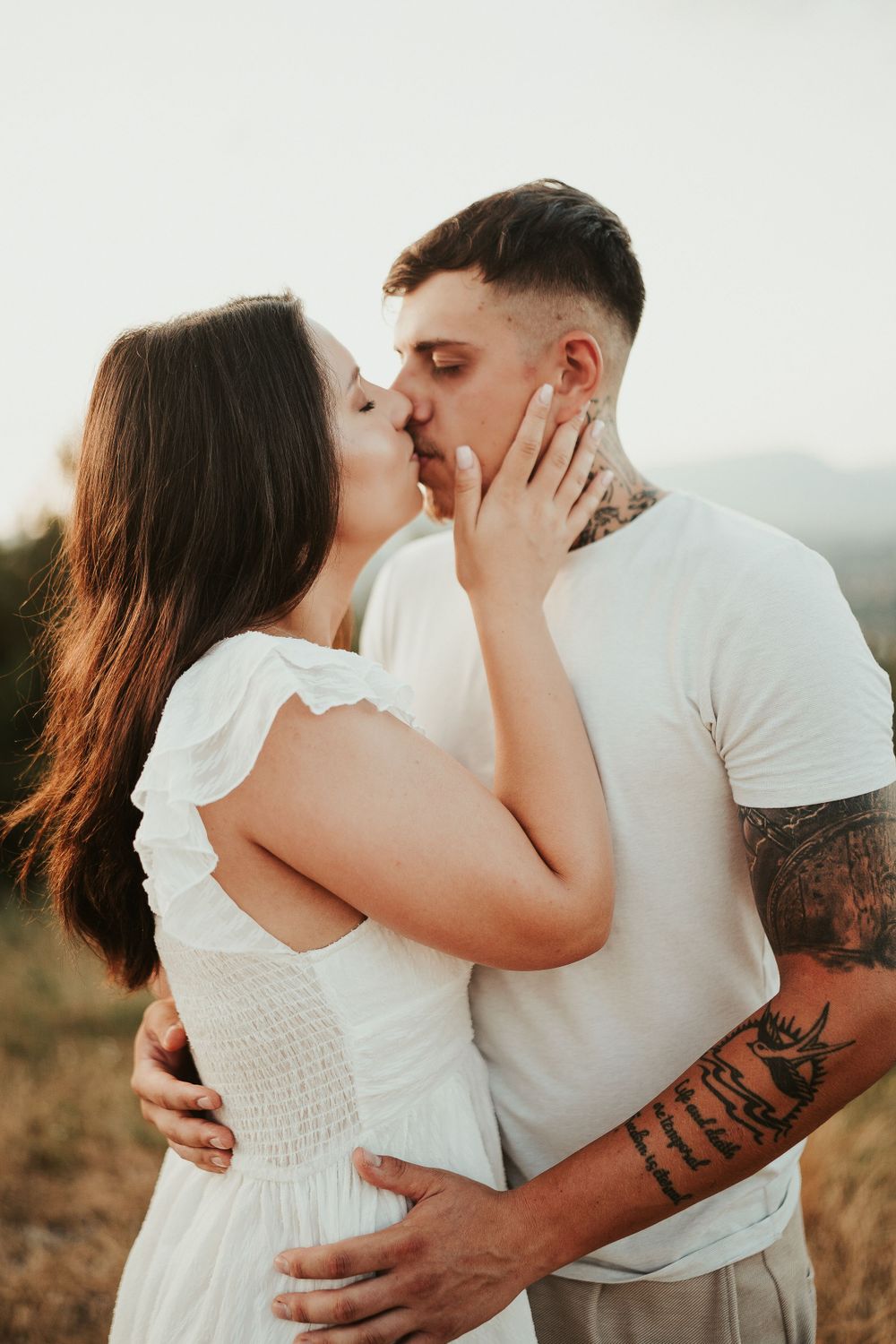 A couple shares a romantic kiss on a mountain overlook during golden hour.