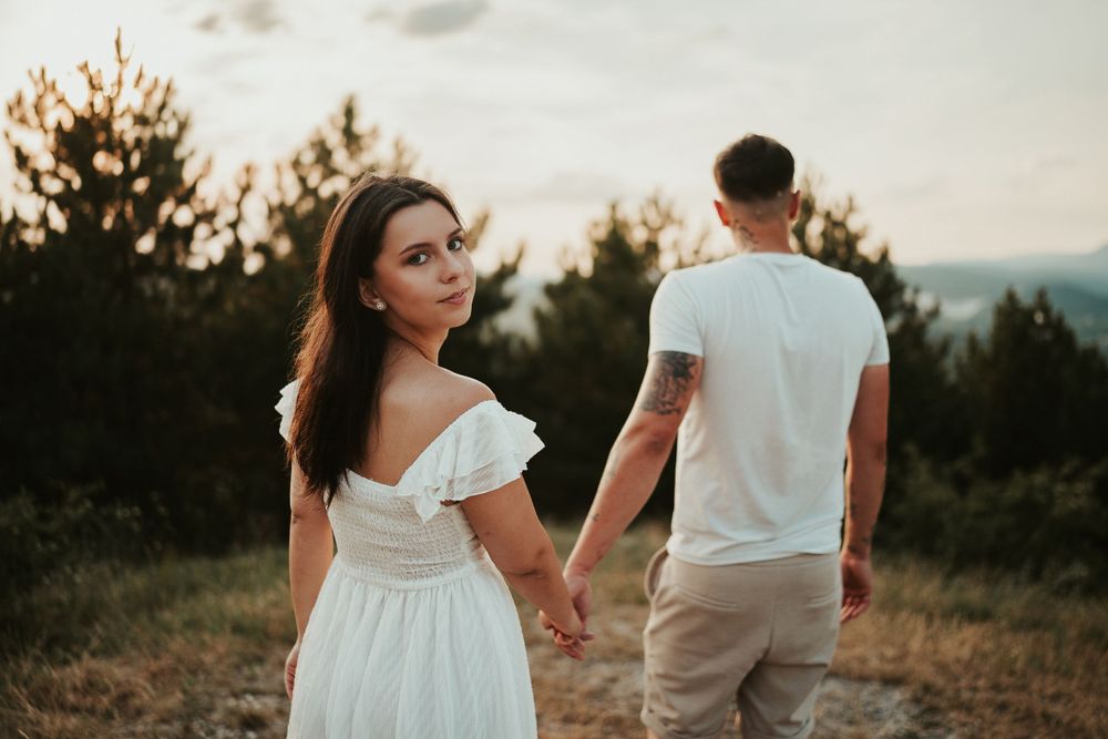 A couple in white outfits walks along a mountain trail during sunset.