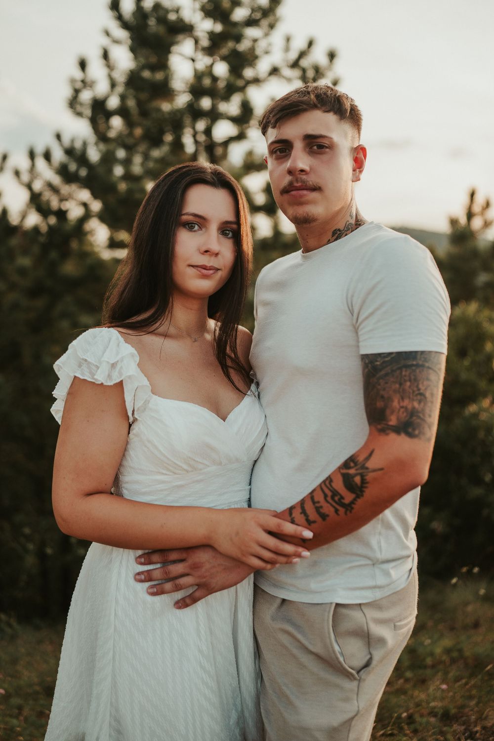 A couple in coordinated white and beige outfits poses together on a mountain overlook.