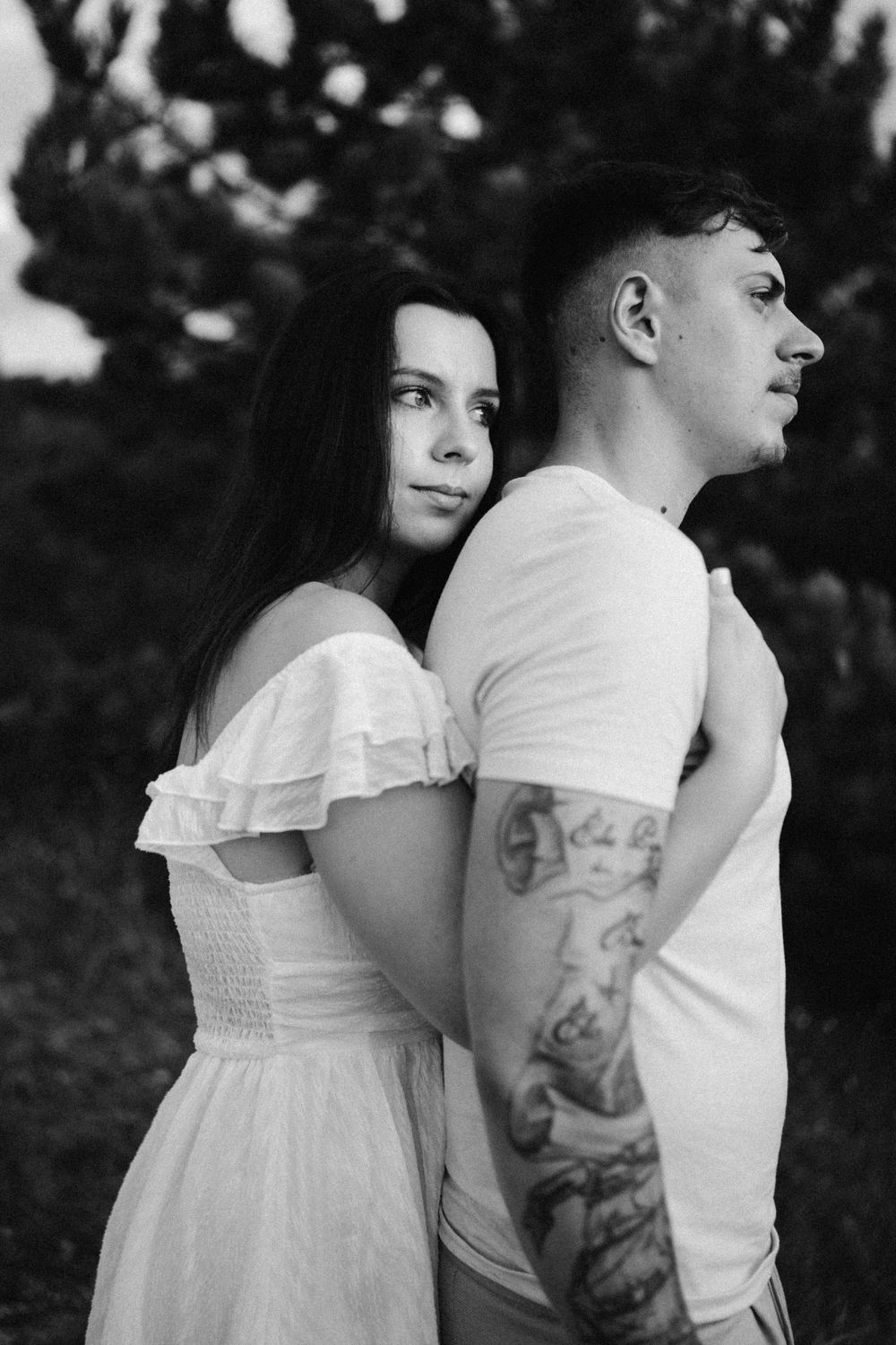 Black and white portrait of couple in white clothing standing back to back in nature.