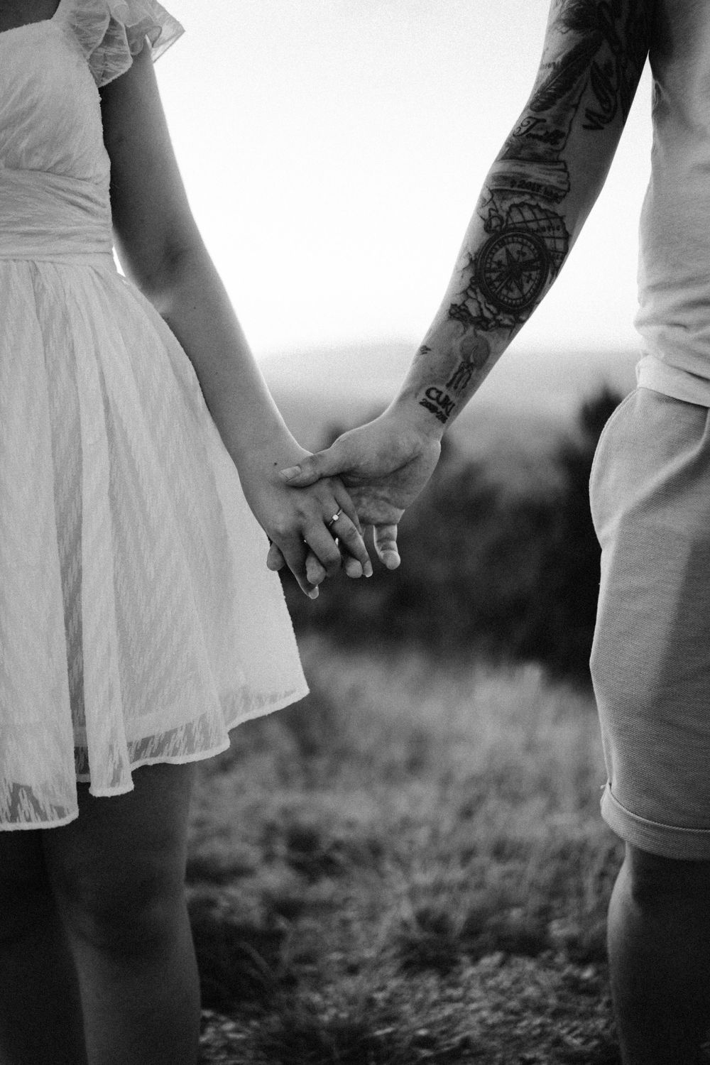 Close-up black and white photo of couple holding hands with woman in white dress.