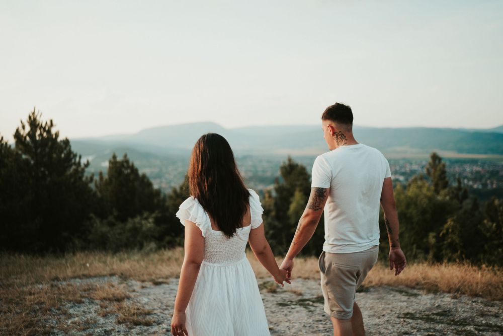 Couple holding hands while walking on mountain overlook during golden hour.