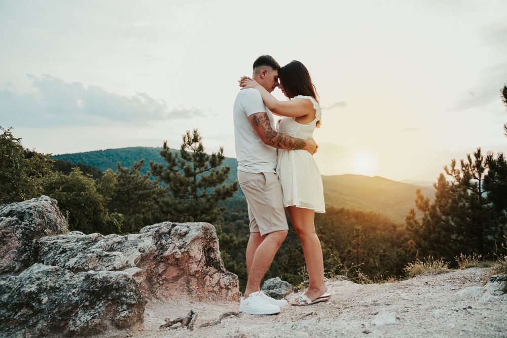 A couple shares an intimate moment while standing on a rocky mountain overlook at sunset.