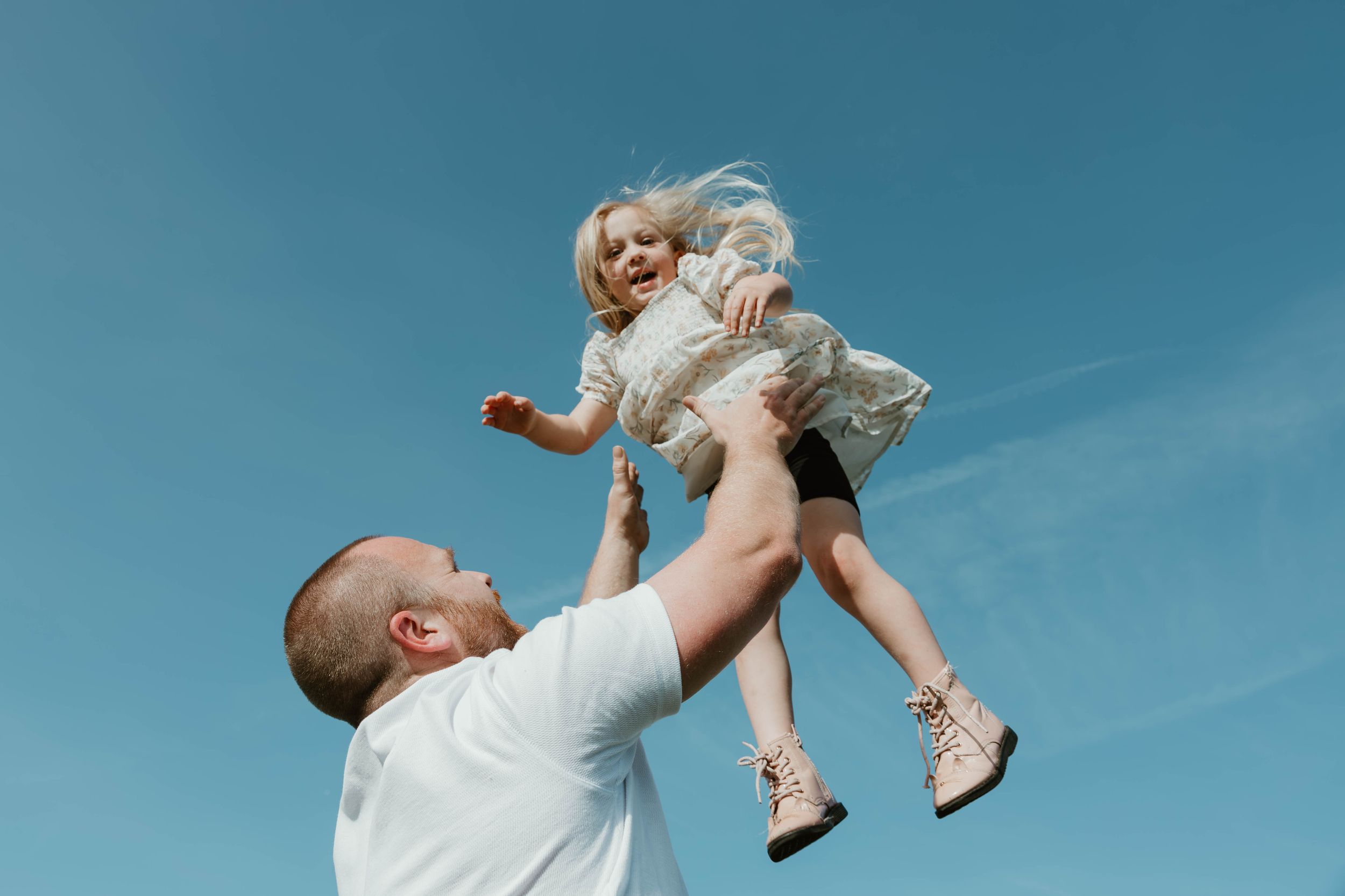 A joyful moment captured as someone lifts a small child high into the bright blue sky.