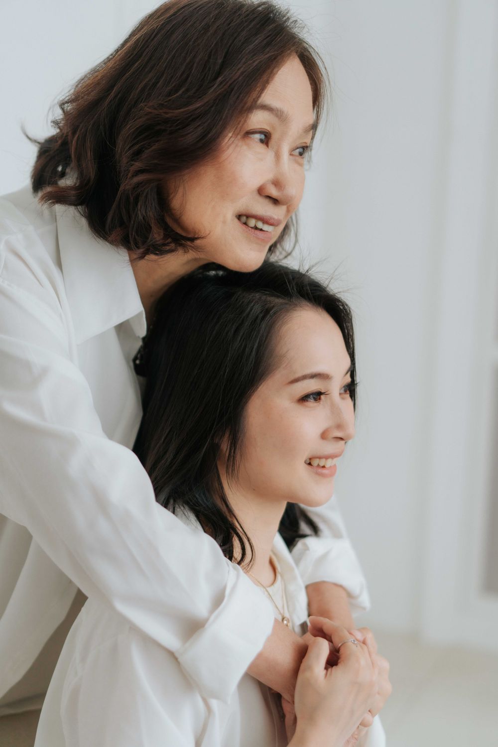 Two people in white shirts embrace and smile warmly in bright minimal setting.