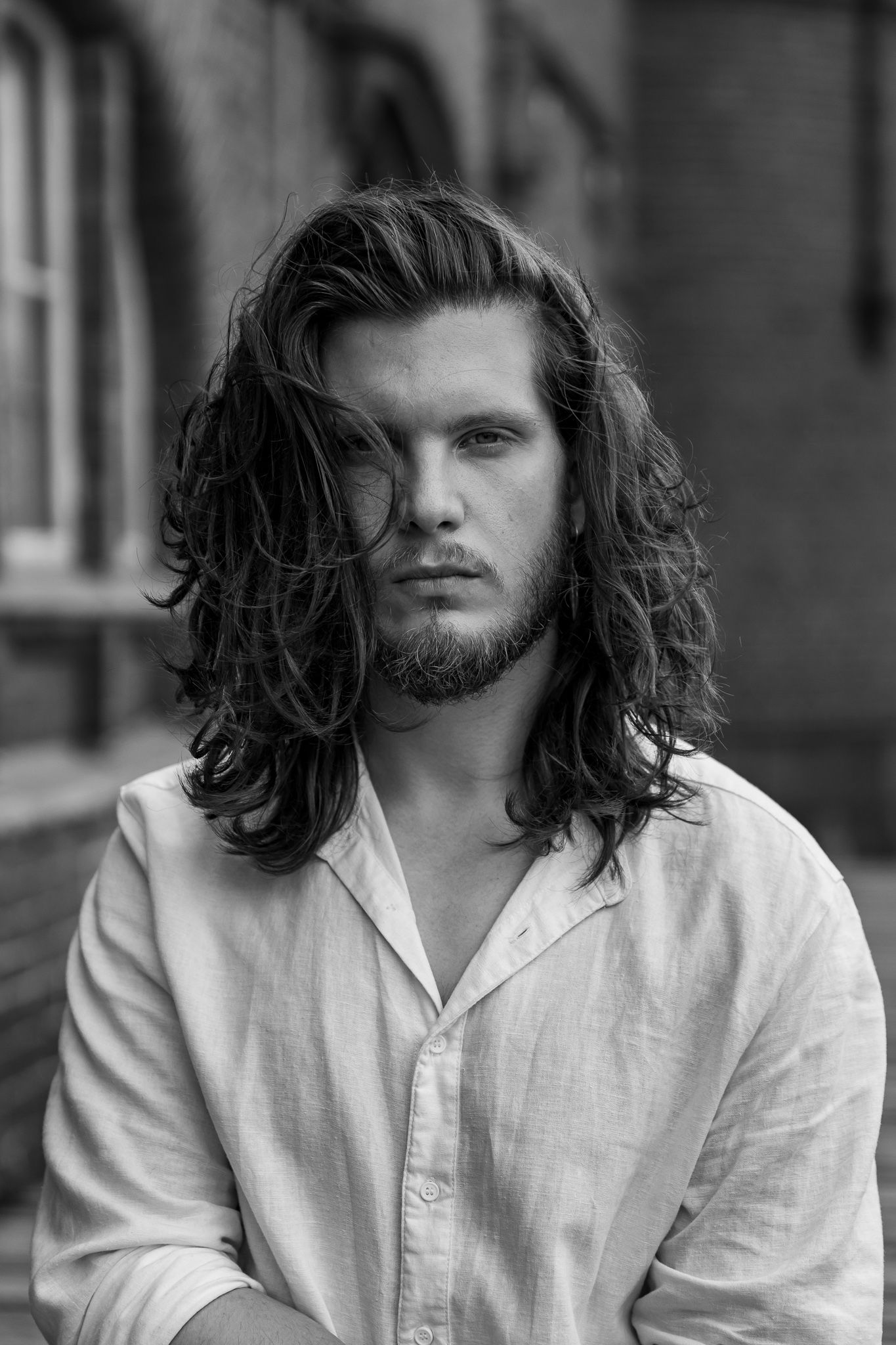 Black and white portrait of man with long wavy dark hair and beard wearing a white button-up shirt.