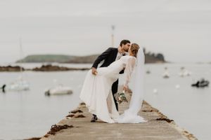 Un couple en tenue de mariage s'embrassant sur une jetée  devant la baie de Lancieux