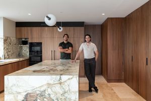 Modern kitchen interior with wood paneled walls and large marble island featuring sleek cabinetry and light oak flooring.