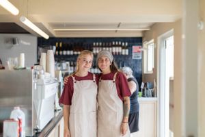 Restaurant staff wearing matching burgundy aprons in kitchen environment.