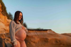 Maternity photo captured against dramatic orange cliffs at sunrise.