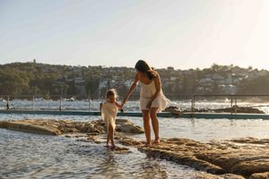 People enjoying a sunset at a scenic rocky beach with boats and harbor views in the background.
