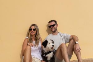 A group of friends sit on steps with a small white dog while wearing casual summer attire.