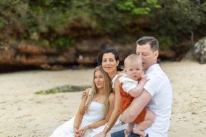 Family group sitting together on a beach with rocky cliffs in the background.