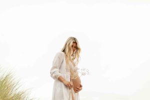 Ethereal outdoor scene with flowing white dress and dried flowers against bright sky.