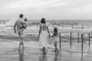 A series of black and white beach photos showing people walking along the shoreline and boardwalk at sunset.