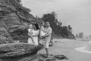 Vintage black and white photograph of two people standing on a rocky beach with waves and cliffs in the background.