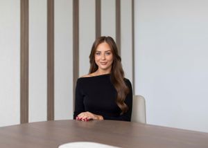Professional woman in black sweater sitting at conference table in modern office setting.