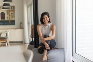 A person in gray clothing sits casually on a windowsill in a bright, modern interior space.